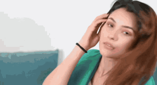 a woman is sitting on a couch talking on a cell phone while touching her hair .