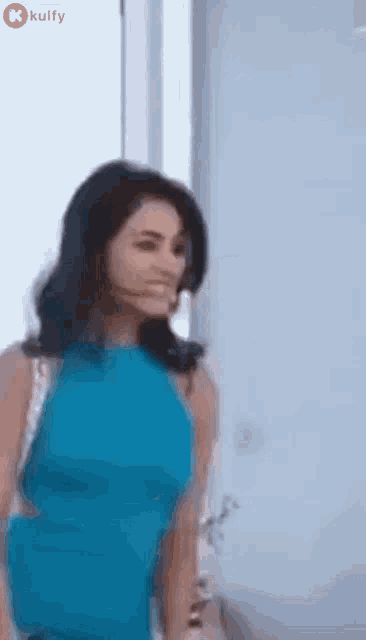 a woman in a blue dress is standing next to a window and smiling .