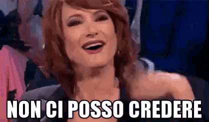 a woman with red hair is smiling in front of a crowd and the words non ci posso credere are above her .