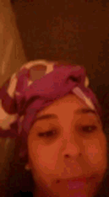 a woman with a pink towel wrapped around her head is looking at the camera .