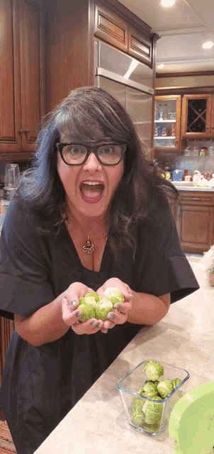 a woman wearing glasses is holding a bowl of brussels sprouts in her hands