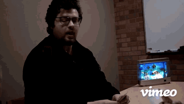 a man sitting at a table with a vimeo logo in the background