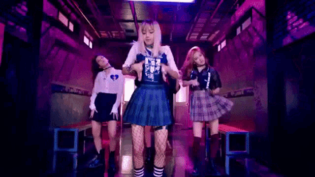 a group of girls are dancing together in a dark room in front of a pink sign .