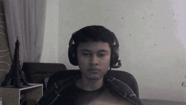 a young man wearing headphones and a plaid shirt looks at the camera