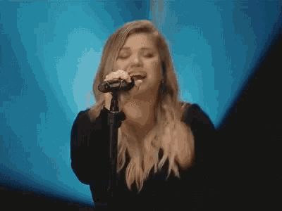 a woman is singing into a microphone on a stage in front of a blue background .