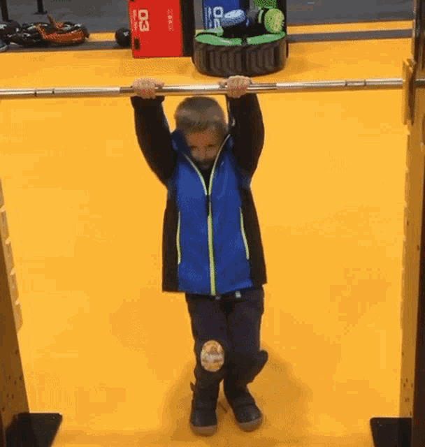 a young boy hangs upside down on a bar with a red box with the number 03 on it behind him