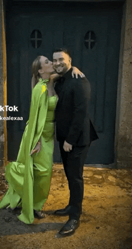 a man and a woman are standing next to each other in front of a door . the woman is wearing a green dress .