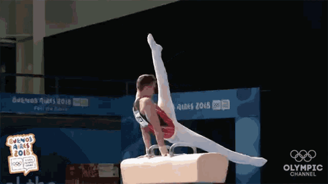 a gymnast performs a trick on a pommel horse in front of a sign that says olympic channel