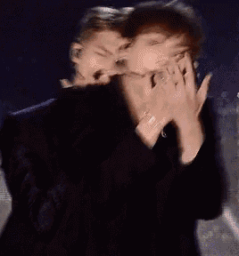 two men are covering their mouths with their hands while standing next to each other on a stage .