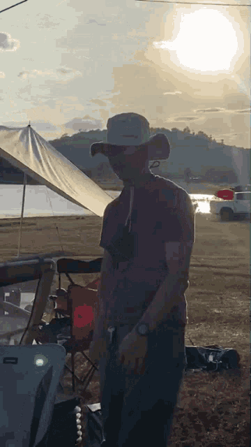 a man in a cowboy hat is standing in a field with a tent in the background