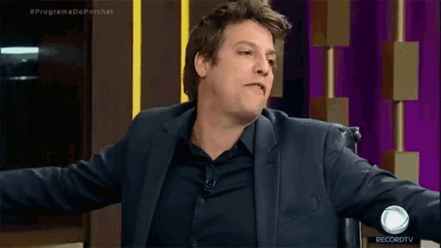 a man in a suit is sitting in a chair with his arms outstretched in front of a record tv logo .
