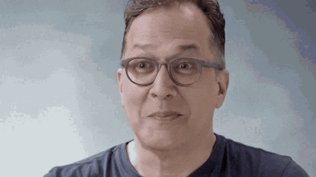 a man wearing glasses and a blue shirt is making a surprised face