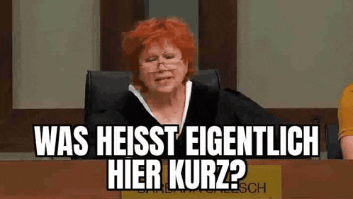 a woman with red hair is sitting at a table with a sign that says was heisst eigentlich hier kurz