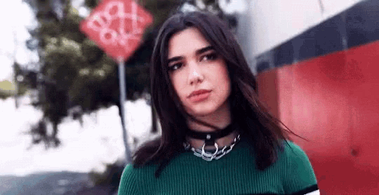 a woman wearing a green sweater and a choker is standing in front of a red street sign .