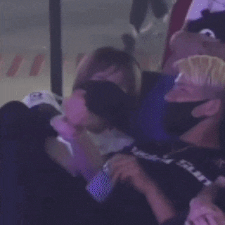 a man wearing a mask is sitting next to a woman in a crowd .