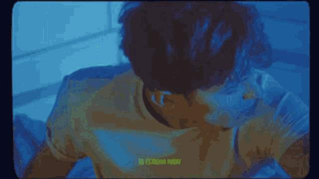 a man in a yellow shirt is sitting in a dark room with a green screen behind him .