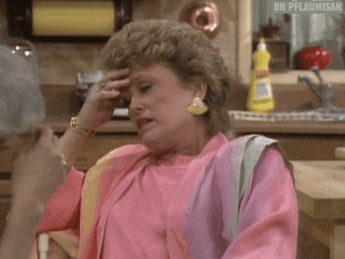a woman in a pink shirt is sitting at a table in a kitchen .