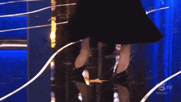 a woman in a black dress is dancing in front of a blue curtain that says mediaset