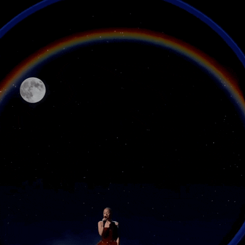 a woman singing in front of a full moon and a rainbow
