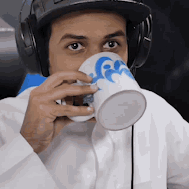 a man wearing headphones and a hat drinks from a white cup with a blue swirl on it