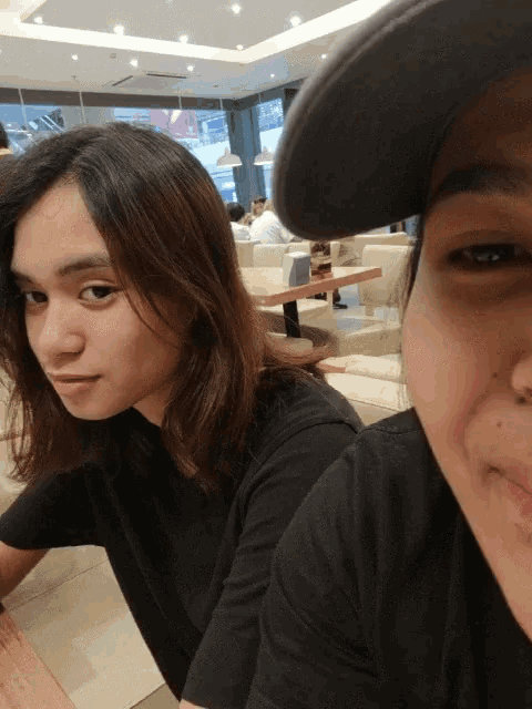 two women are sitting at a table in a restaurant and one is wearing a hat