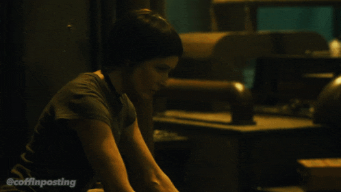 a woman sits in a dark room with the hashtag coffinposting