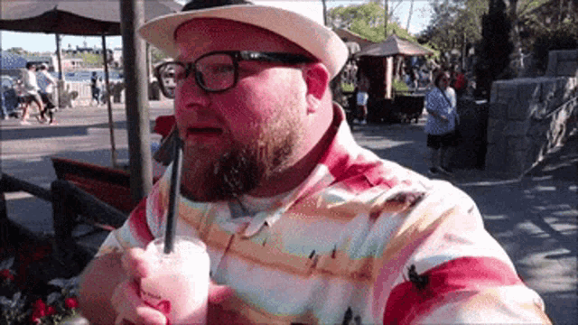 a man wearing a hat and glasses is drinking a pink drink with a straw