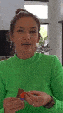 a woman in a neon green sweater is holding a candy bar in her hands .