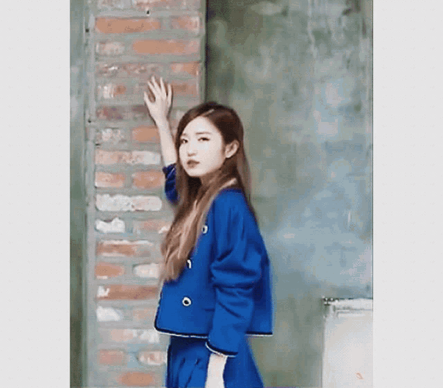 a woman in a blue jacket is standing in front of a brick wall