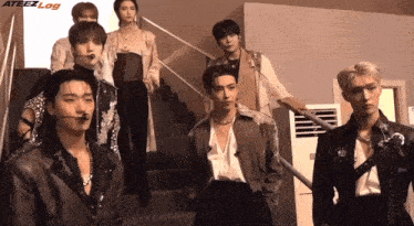 a group of young men standing next to each other in front of stairs with the word ateezlog on the bottom right
