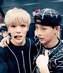 two young men are standing next to each other and one is wearing a hat with a spider web on it .