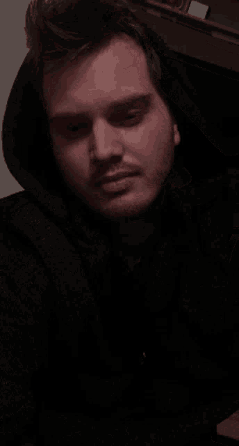 a man wearing a black hoodie looks at the camera with his eyes closed