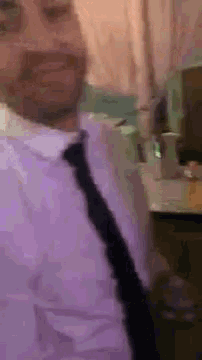 a man wearing a purple shirt and black tie is standing in front of a desk .