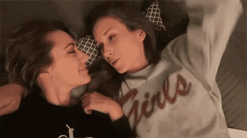 two women are laying on a bed kissing each other .