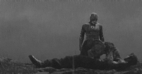a black and white photo of a man in a superhero costume standing next to another man in the rain .