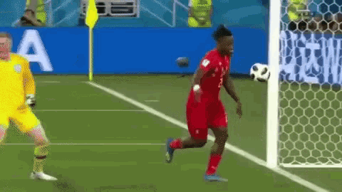 a soccer player is running towards a goal while a goalie watches .