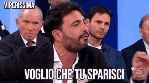 a man with a beard is saying " voglio che tu sparisci " in front of a group of people
