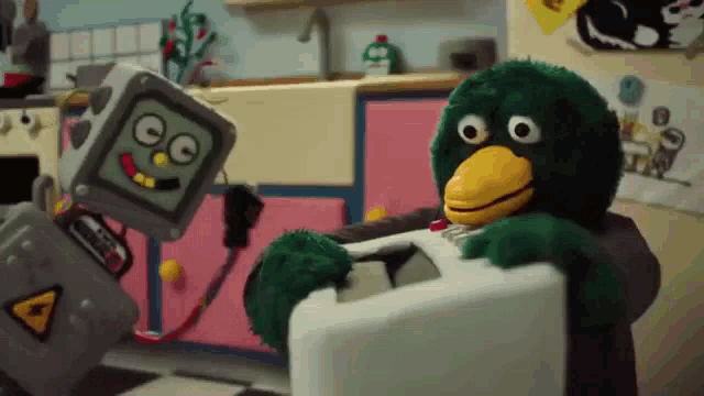 two stuffed animals are standing next to each other in a kitchen . one is a robot and the other is a bird .