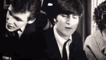 a black and white photo of a man in a suit and tie talking to another man .