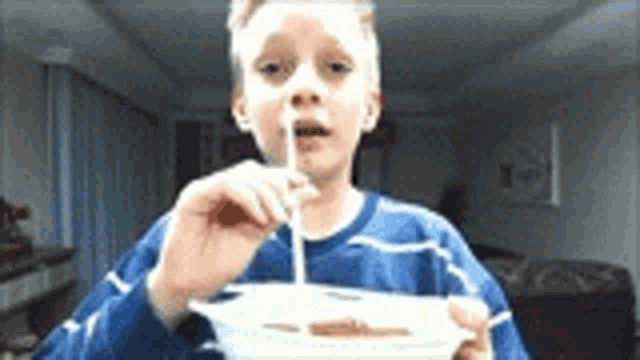 a young boy in a blue shirt is eating food with a spoon .