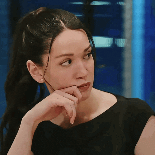 a woman in a black dress has her hand on her face