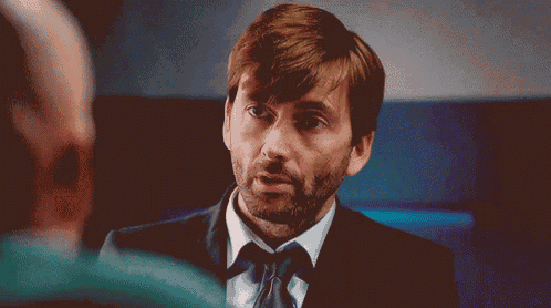 a man in a suit and tie is talking to another man in a room .