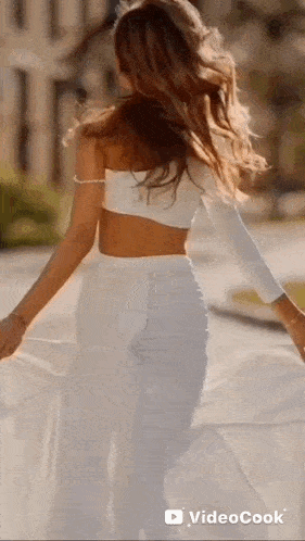 a woman in a white crop top and white pants is walking down a street .