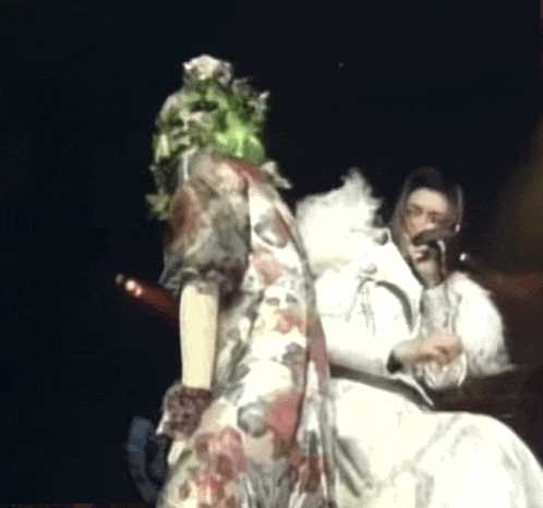 a woman in a floral dress is standing next to a man in a white fur coat holding a microphone .