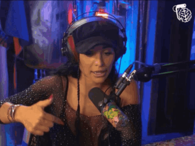 a woman wearing headphones and a hat stands in front of a microphone giving a thumbs up