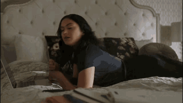 a woman is laying on a bed looking at a laptop computer .