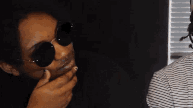 a woman wearing round sunglasses covering her mouth
