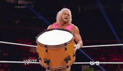 a man in a pink shirt is holding a large drum in a wrestling ring