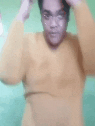 a man in a yellow sweater is making a funny face with his hands .