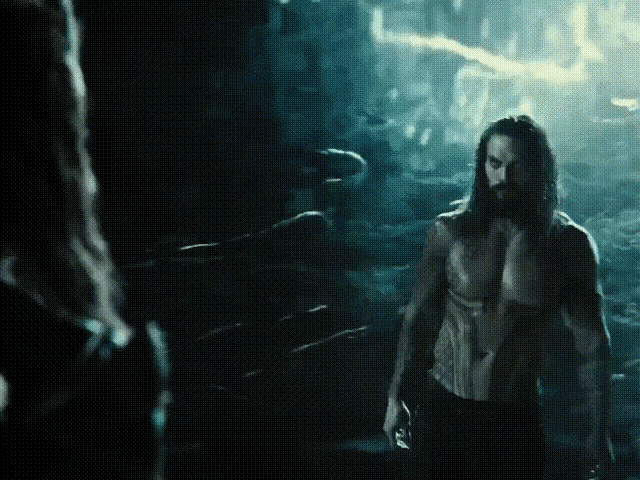 a man with long hair and a beard stands in a dark room